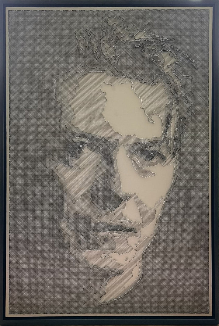 Portrait of David Bowie constructed from fine black enamelled copper wire tensioned around thousands of small metal nails on a silver acrylic painted board, forming dense linear layers that define facial features, hair and expression through tonal variation, depth and shadow across a rigid rectangular surface.