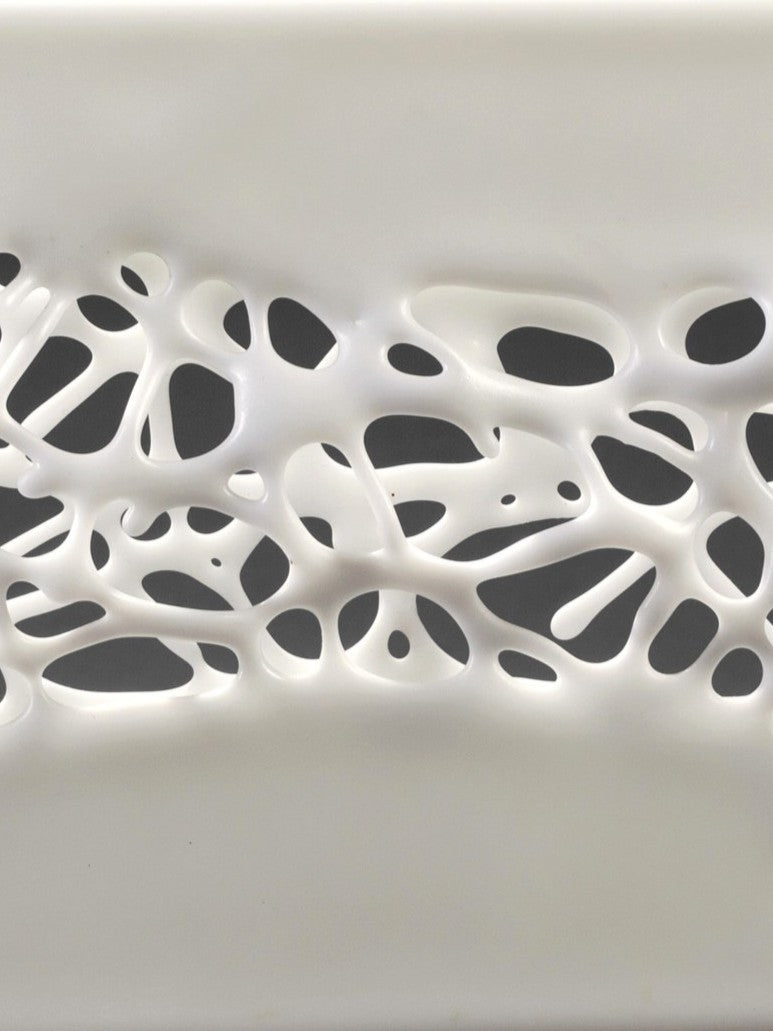 Diaphaneity VIII by Tracy Nicholls — a one-off kiln-formed glass and marble sculpture. Two panels of opaque white glass rest on a marble base, their surface pierced by an intricate lace-like web that seems to dissolve into open space. The organic strands ripple with gentle movement, allowing light to filter through and cast shifting shadows across surrounding surfaces, transforming solidity into a play of fragility and air.