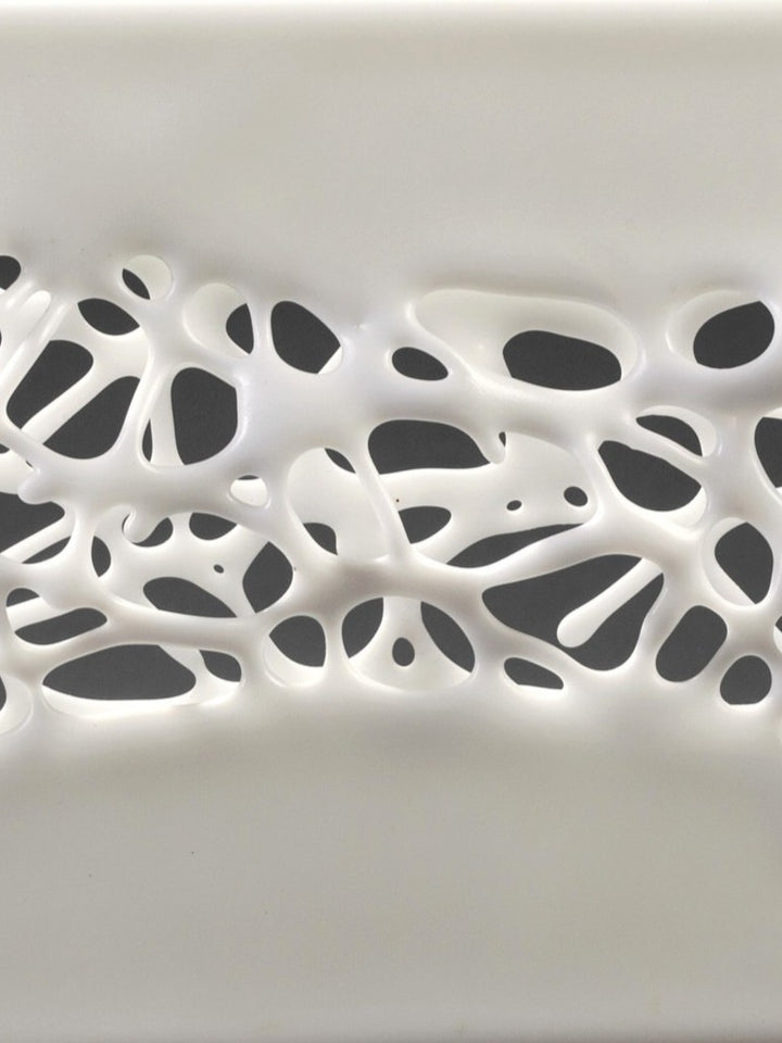 Diaphaneity VIII by Tracy Nicholls — a one-off kiln-formed glass and marble sculpture. Two panels of opaque white glass rest on a marble base, their surface pierced by an intricate lace-like web that seems to dissolve into open space. The organic strands ripple with gentle movement, allowing light to filter through and cast shifting shadows across surrounding surfaces, transforming solidity into a play of fragility and air.