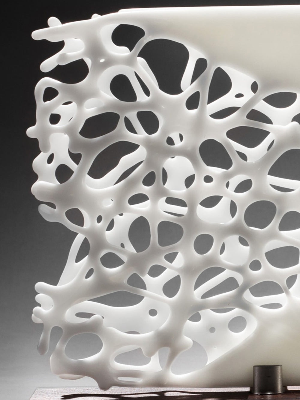 Diaphaneity VIII by Tracy Nicholls — a one-off kiln-formed glass and marble sculpture. Two panels of opaque white glass rest on a marble base, their surface pierced by an intricate lace-like web that seems to dissolve into open space. The organic strands ripple with gentle movement, allowing light to filter through and cast shifting shadows across surrounding surfaces, transforming solidity into a play of fragility and air.