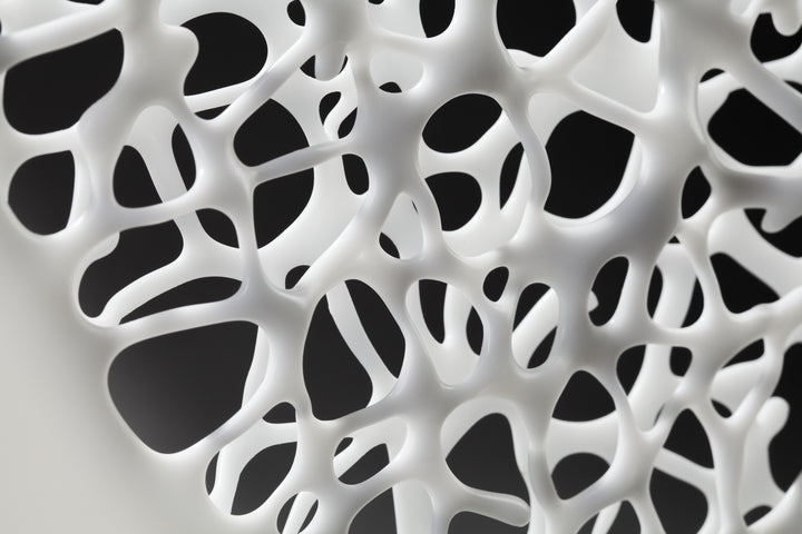 Diaphaneity VIII by Tracy Nicholls — a one-off kiln-formed glass and marble sculpture. Two panels of opaque white glass rest on a marble base, their surface pierced by an intricate lace-like web that seems to dissolve into open space. The organic strands ripple with gentle movement, allowing light to filter through and cast shifting shadows across surrounding surfaces, transforming solidity into a play of fragility and air.