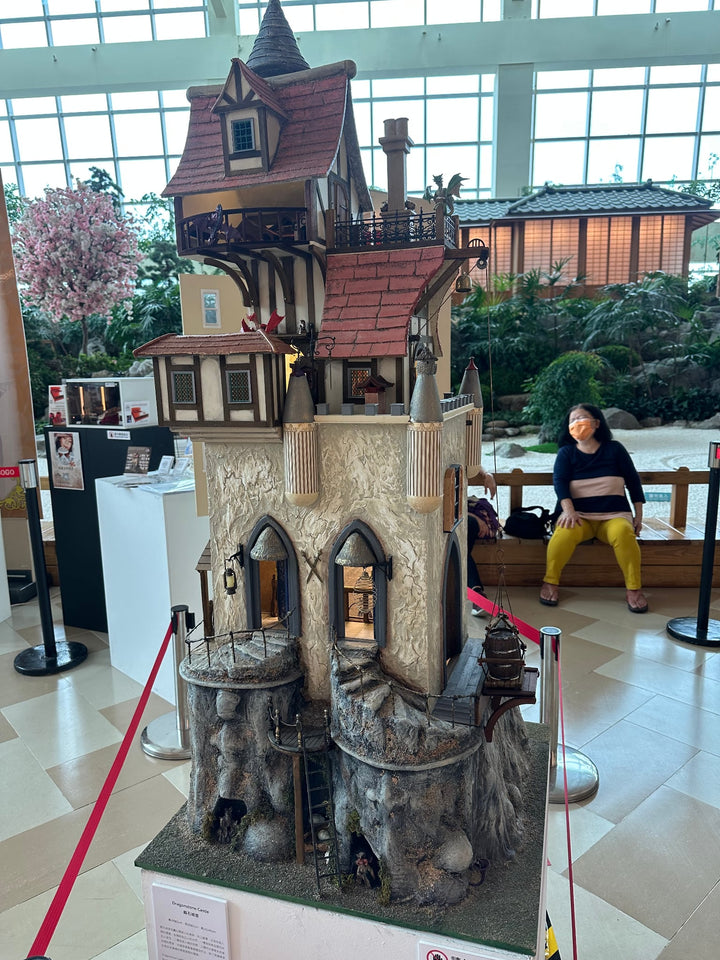Handcrafted fantasy-style dolls house with a steep gabled roof, stone base, and intricate Tudor details on multiple levels.