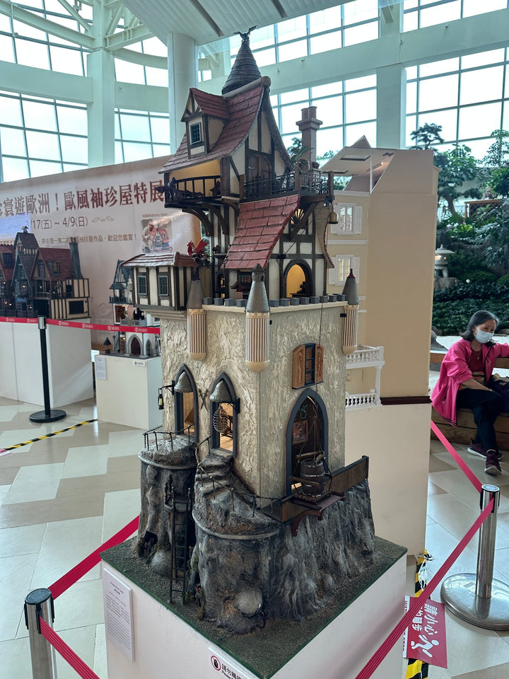Handcrafted fantasy-style dolls house with a steep gabled roof, stone base, and intricate Tudor details on multiple levels.