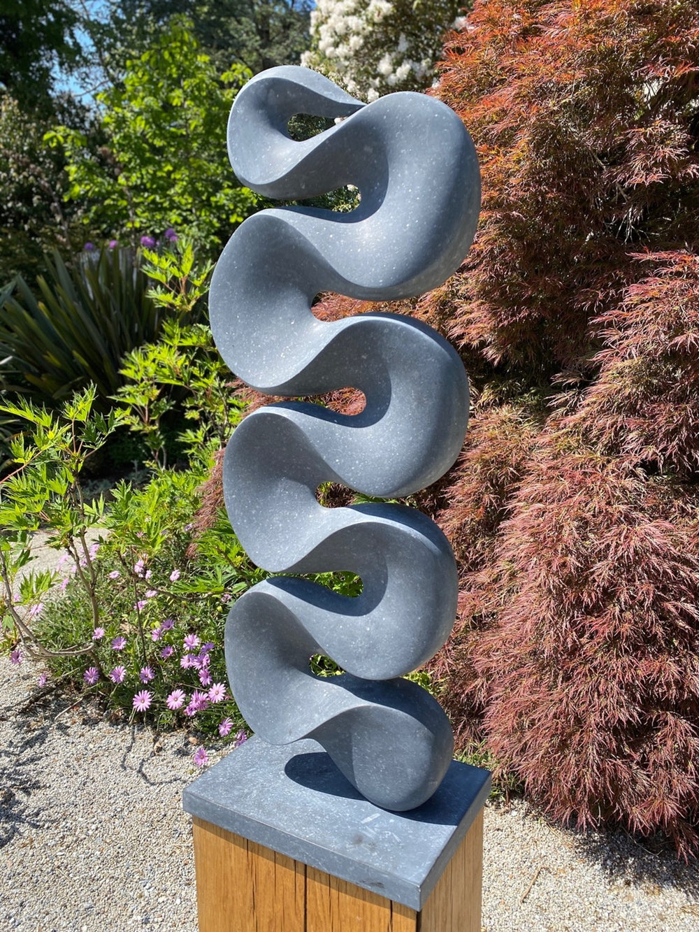 Abstract stone sculpture Ebb & Flow – 2025 by Hamish Holman, carved in deep grey Kilkenny limestone with a tall vertical form of flowing wave-like curves, smooth polished surface with subtle flecks of light grey, mounted on a stone base.