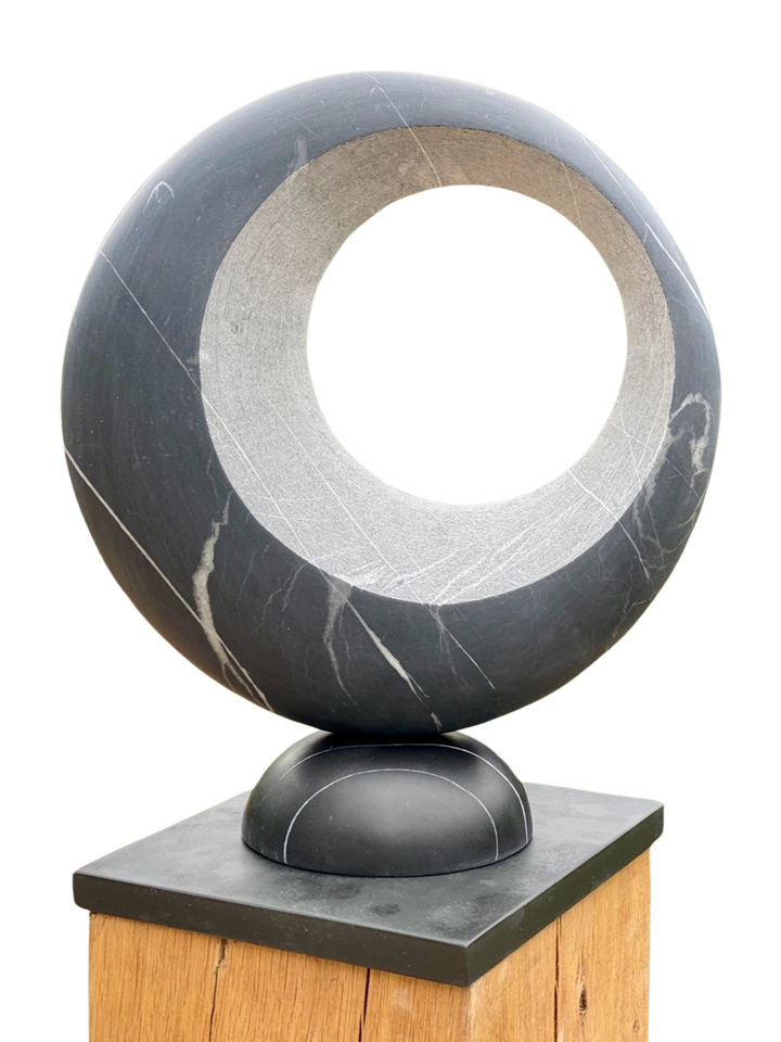 Abstract stone sculpture Eclipse – 2025 by Hamish Holman, carved from Nero Blue marble with a smooth circular form and hollowed centre, featuring natural white veining and a polished dark blue-grey surface, mounted on a wooden plinth.