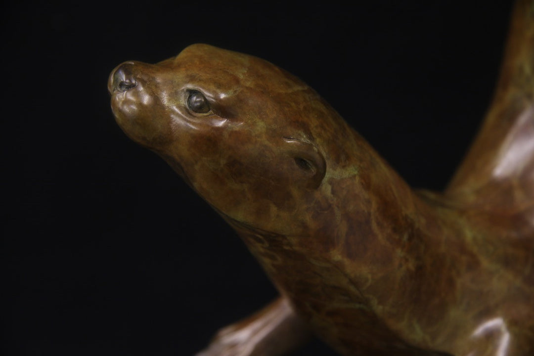 Bronze sculpture of a single otter diving with fluid, spiral movement, set against a black background.
