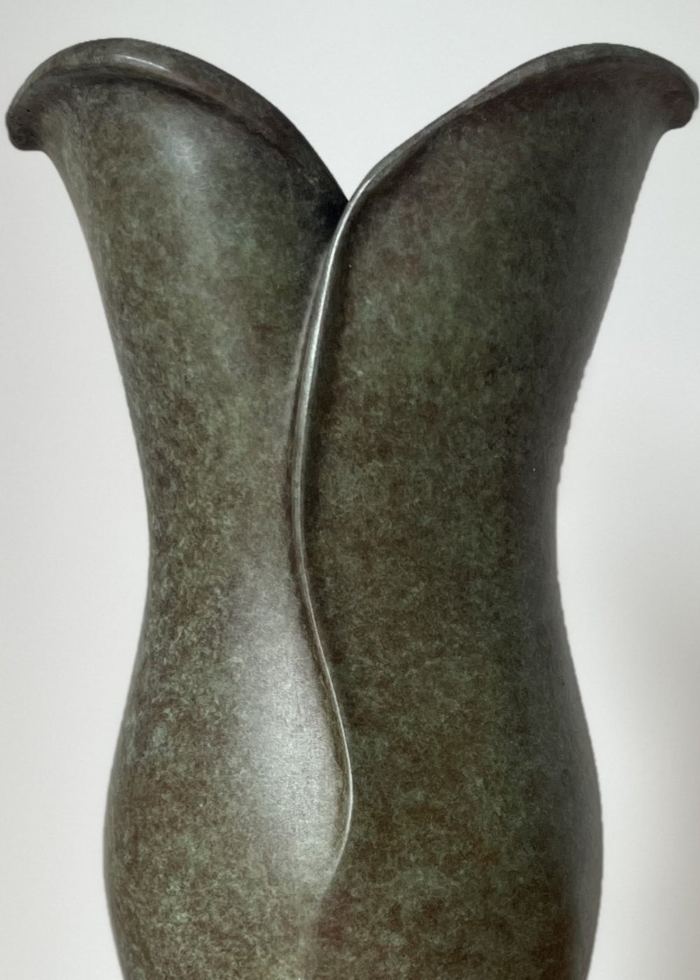 Small bronze sculpture with soft, organic curves that rise and part at the top like unfolding petals, finished in a mottled green and earthy brown patina, set on a polished black stone base.