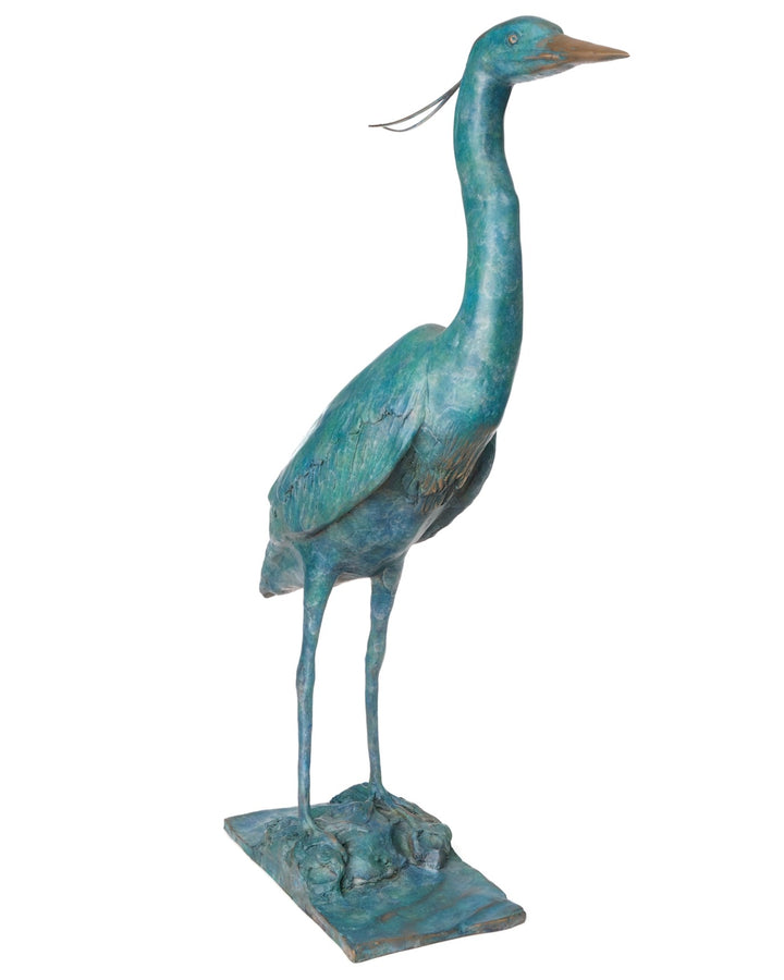‘Erodios’ by Pat Bull, a limited-edition life-size bronze wildlife sculpture depicting a heron standing upright with an elongated curved neck, slender legs, pointed bronze beak and finely textured folded wings. Finished in a rich turquoise, teal and blue-green verdigris patina with subtle earthy bronze highlights, the bird features delicate trailing head feathers and stands on a rectangular naturalistic bronze base with sculpted rocks, capturing the graceful appearance of this distinctive wading bird.