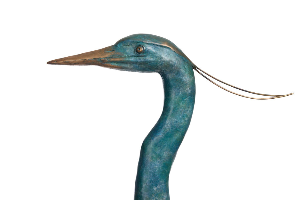 ‘Erodios’ by Pat Bull, a limited-edition life-size bronze wildlife sculpture depicting a heron standing upright with an elongated curved neck, slender legs, pointed bronze beak and finely textured folded wings. Finished in a rich turquoise, teal and blue-green verdigris patina with subtle earthy bronze highlights, the bird features delicate trailing head feathers and stands on a rectangular naturalistic bronze base with sculpted rocks, capturing the graceful appearance of this distinctive wading bird.