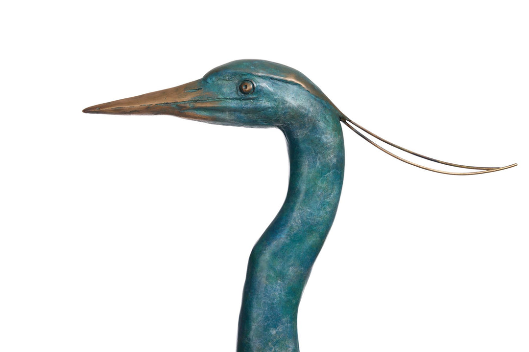 ‘Erodios’ by Pat Bull, a limited-edition life-size bronze wildlife sculpture depicting a heron standing upright with an elongated curved neck, slender legs, pointed bronze beak and finely textured folded wings. Finished in a rich turquoise, teal and blue-green verdigris patina with subtle earthy bronze highlights, the bird features delicate trailing head feathers and stands on a rectangular naturalistic bronze base with sculpted rocks, capturing the graceful appearance of this distinctive wading bird.