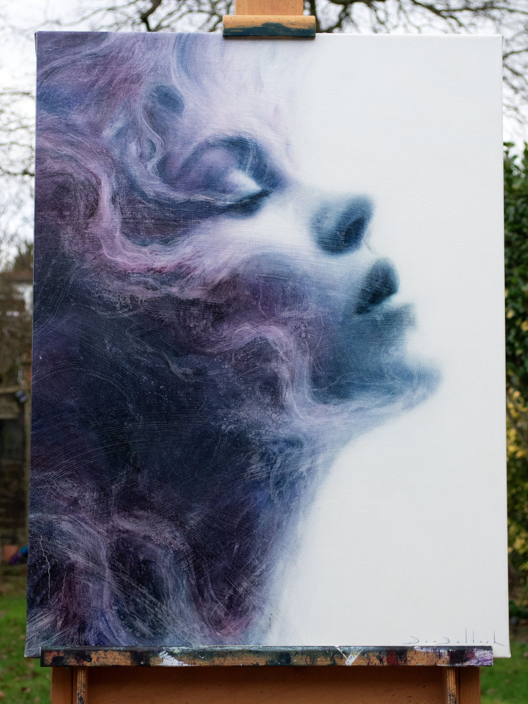 Oil on canvas painting by Dan Bullock, titled Eternal. A dreamlike portrait of a woman’s face in profile, eyes closed, emerging from swirling textures of deep indigo, violet, and soft lavender. The ethereal brushwork gives the impression of smoke or mist, creating a sense of serenity, timelessness, and transcendence.