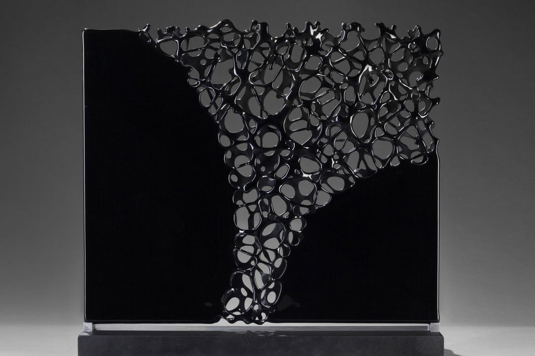 Tracy Nicholls glass sculpture Ethereality — a one-off kiln-formed artwork of opaque black glass with lace-like webbing that dissolves into open apertures. Standing on a granite and metal base, the intricate strands create depth and movement, while light filters through the perforations to cast shifting shadows.