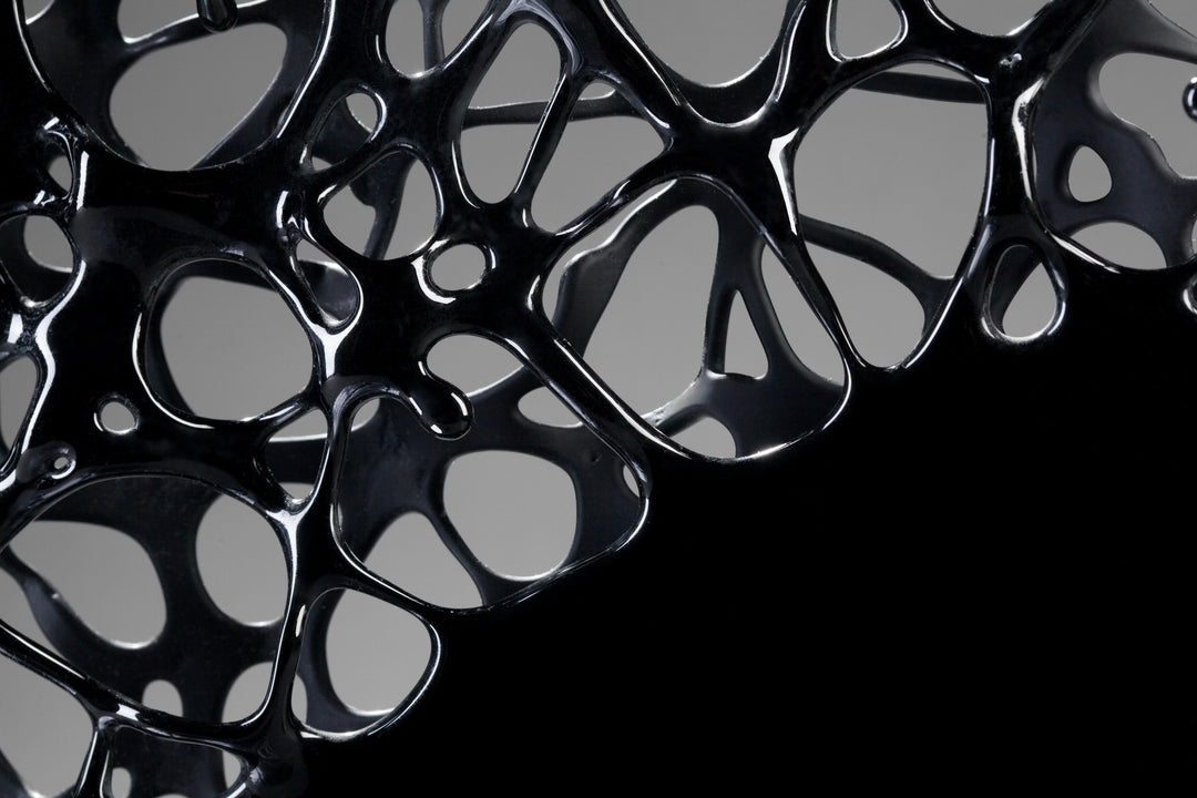 Tracy Nicholls glass sculpture Ethereality — a one-off kiln-formed artwork of opaque black glass with lace-like webbing that dissolves into open apertures. Standing on a granite and metal base, the intricate strands create depth and movement, while light filters through the perforations to cast shifting shadows.