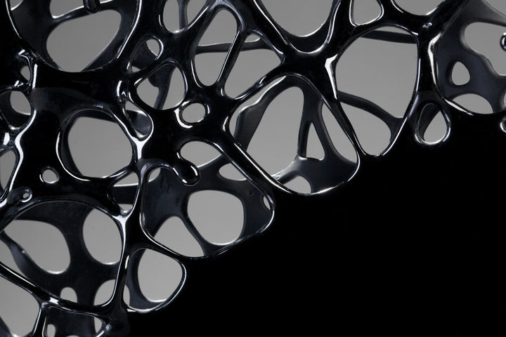 Tracy Nicholls glass sculpture Ethereality — a one-off kiln-formed artwork of opaque black glass with lace-like webbing that dissolves into open apertures. Standing on a granite and metal base, the intricate strands create depth and movement, while light filters through the perforations to cast shifting shadows.