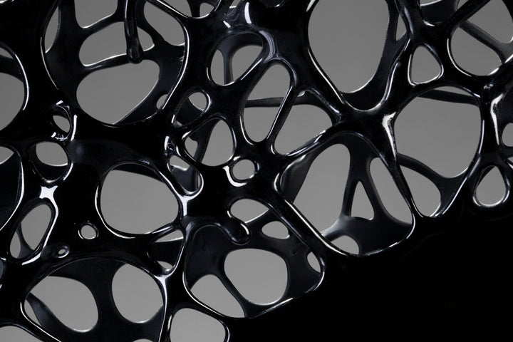 Tracy Nicholls glass sculpture Ethereality — a one-off kiln-formed artwork of opaque black glass with lace-like webbing that dissolves into open apertures. Standing on a granite and metal base, the intricate strands create depth and movement, while light filters through the perforations to cast shifting shadows.