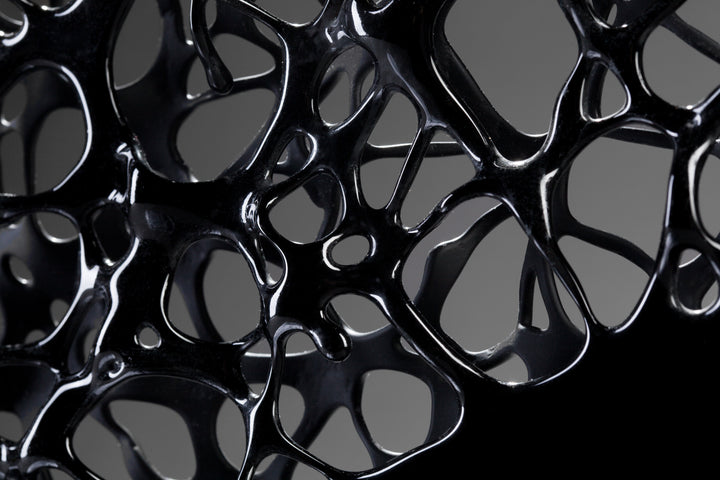 Tracy Nicholls glass sculpture Ethereality — a one-off kiln-formed artwork of opaque black glass with lace-like webbing that dissolves into open apertures. Standing on a granite and metal base, the intricate strands create depth and movement, while light filters through the perforations to cast shifting shadows.