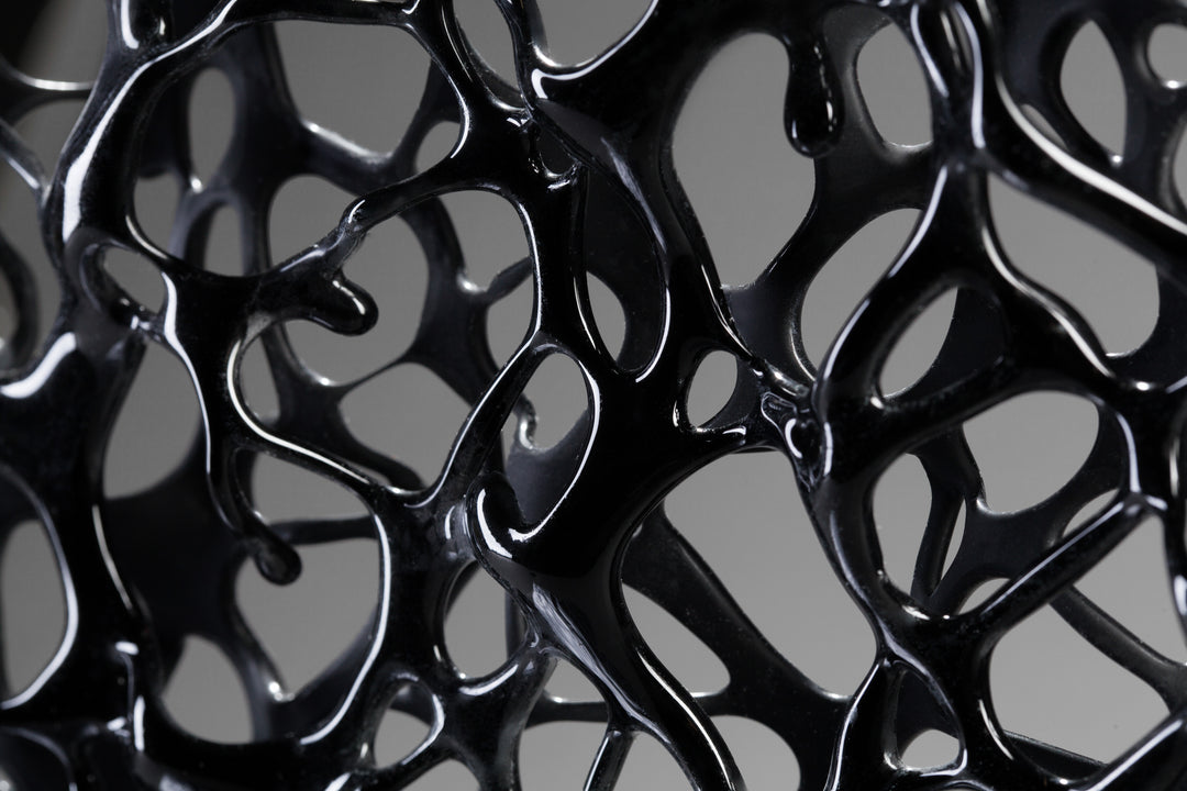 Tracy Nicholls glass sculpture Ethereality — a one-off kiln-formed artwork of opaque black glass with lace-like webbing that dissolves into open apertures. Standing on a granite and metal base, the intricate strands create depth and movement, while light filters through the perforations to cast shifting shadows.