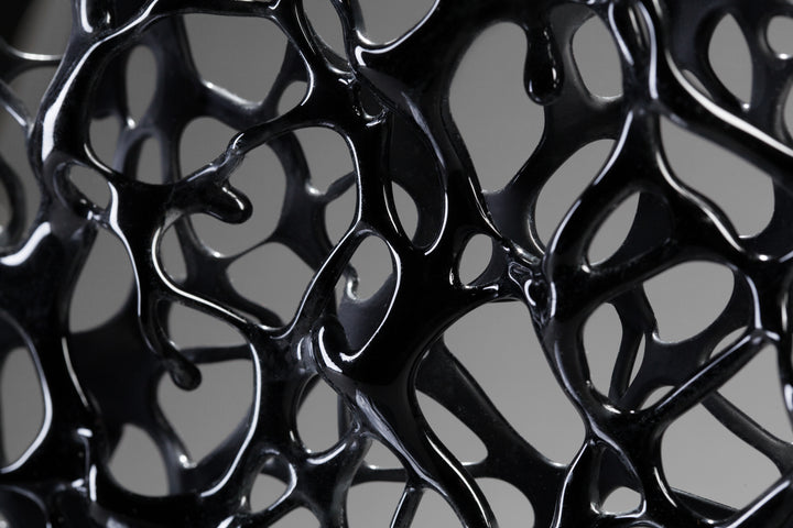 Tracy Nicholls glass sculpture Ethereality — a one-off kiln-formed artwork of opaque black glass with lace-like webbing that dissolves into open apertures. Standing on a granite and metal base, the intricate strands create depth and movement, while light filters through the perforations to cast shifting shadows.