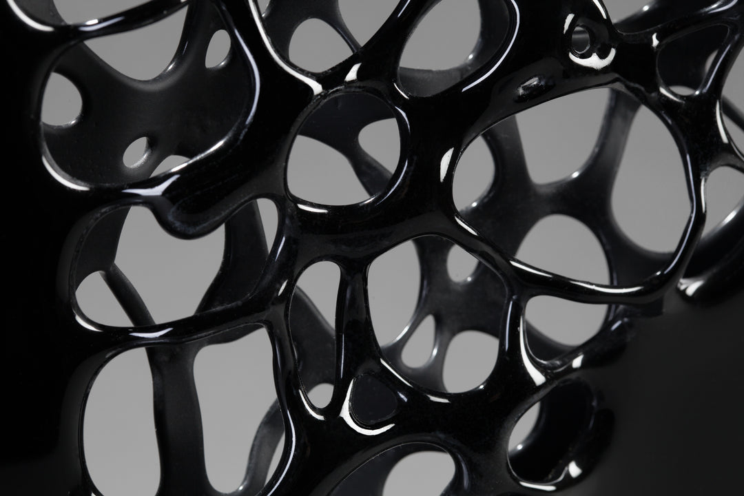 Tracy Nicholls glass sculpture Ethereality — a one-off kiln-formed artwork of opaque black glass with lace-like webbing that dissolves into open apertures. Standing on a granite and metal base, the intricate strands create depth and movement, while light filters through the perforations to cast shifting shadows.