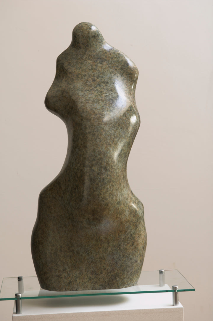 Bronze sculpture of an abstract female torso by Nicola Godden, with smooth organic curves and a softly polished surface, standing on a plinth outdoors against a clear blue sky, the form evoking the human body through simplified, flowing contours and natural balance.