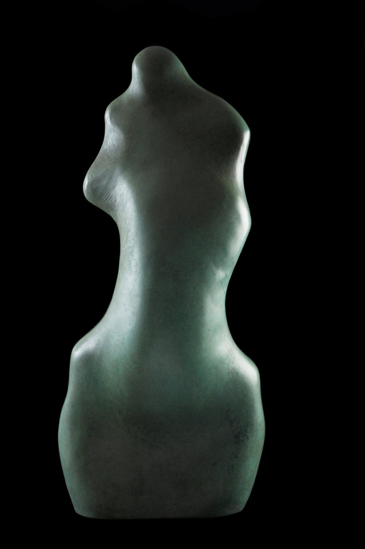 Bronze sculpture of an abstract female torso by Nicola Godden, with smooth organic curves and a softly polished surface, standing on a plinth outdoors against a clear blue sky, the form evoking the human body through simplified, flowing contours and natural balance.