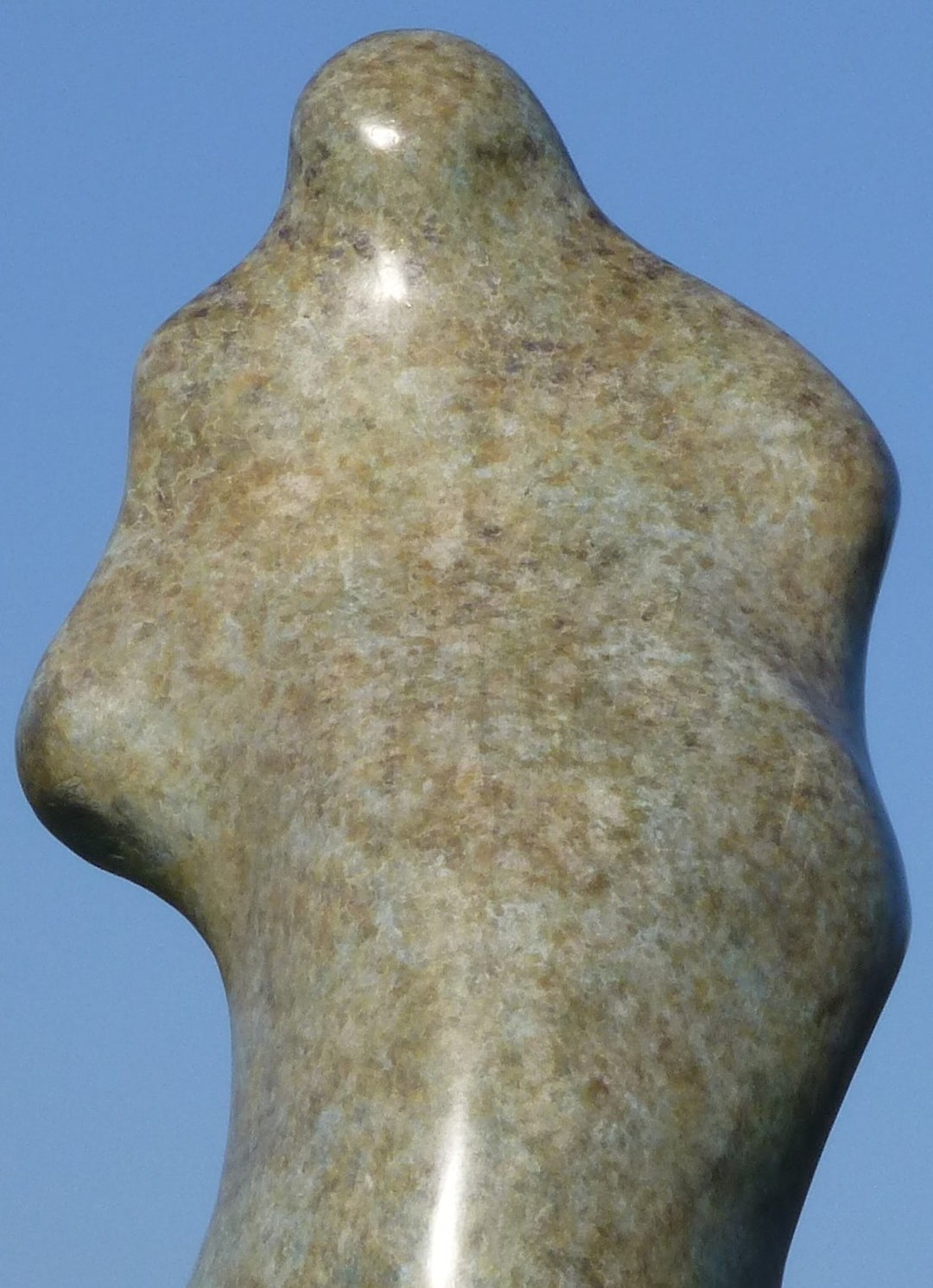 Bronze sculpture of an abstract female torso by Nicola Godden, with smooth organic curves and a softly polished surface, standing on a plinth outdoors against a clear blue sky, the form evoking the human body through simplified, flowing contours and natural balance.