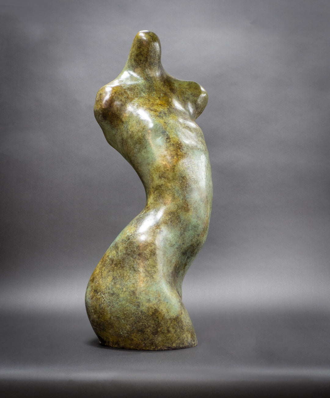 Bronze abstract female torso sculpture by Nicola Godden, with softly curved organic form and smooth hand-finished surface, standing on a plinth outdoors, evoking sensuality, balance and metamorphosis through simplified human anatomy and tactile patination.