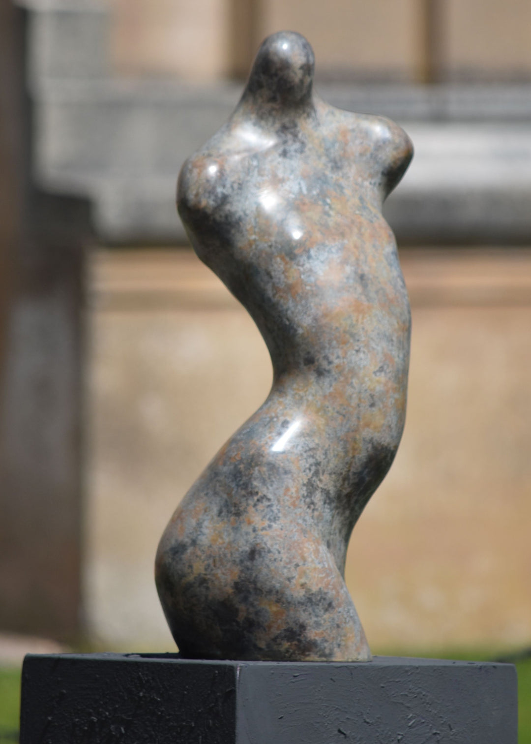 Bronze abstract female torso sculpture by Nicola Godden, with softly curved organic form and smooth hand-finished surface, standing on a plinth outdoors, evoking sensuality, balance and metamorphosis through simplified human anatomy and tactile patination.