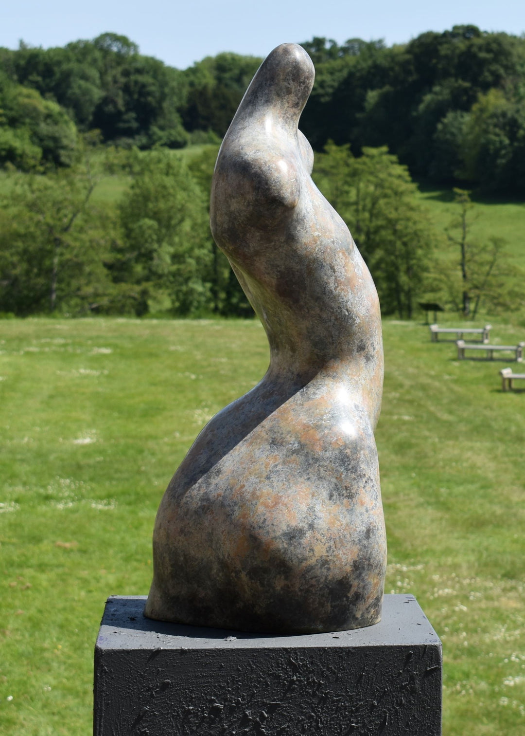 Bronze abstract female torso sculpture by Nicola Godden, with softly curved organic form and smooth hand-finished surface, standing on a plinth outdoors, evoking sensuality, balance and metamorphosis through simplified human anatomy and tactile patination.