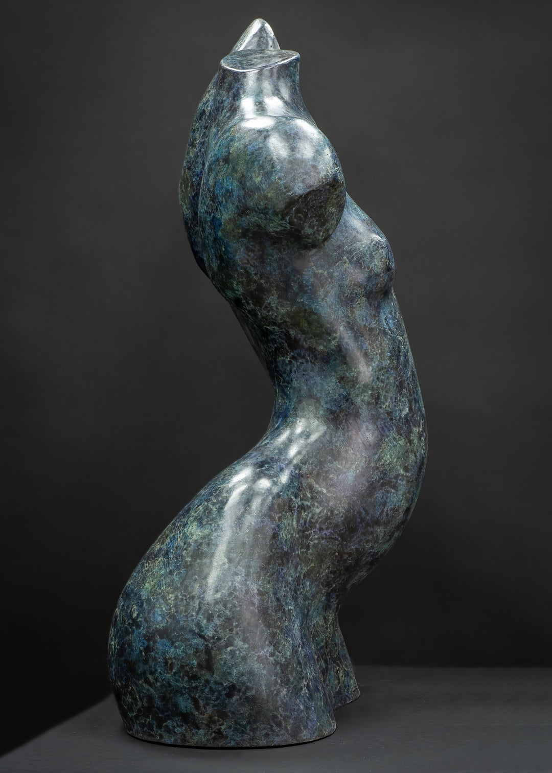 Abstract bronze female torso sculpture by Nicola Godden with flowing organic curves and a polished blue-green patina, standing as a sensual contemporary figurative form designed for garden or exterior display.