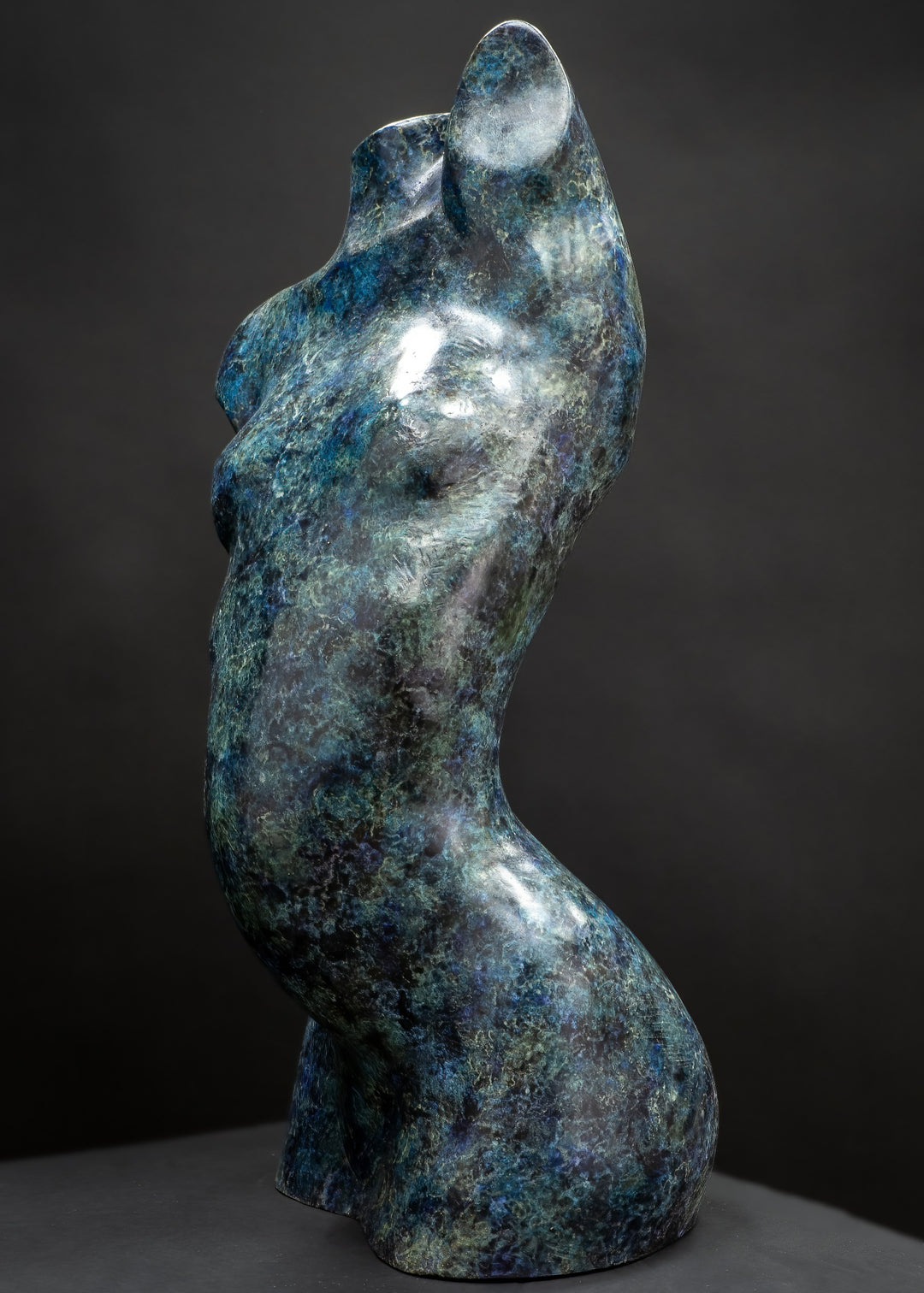 Abstract bronze female torso sculpture by Nicola Godden with flowing organic curves and a polished blue-green patina, standing as a sensual contemporary figurative form designed for garden or exterior display.