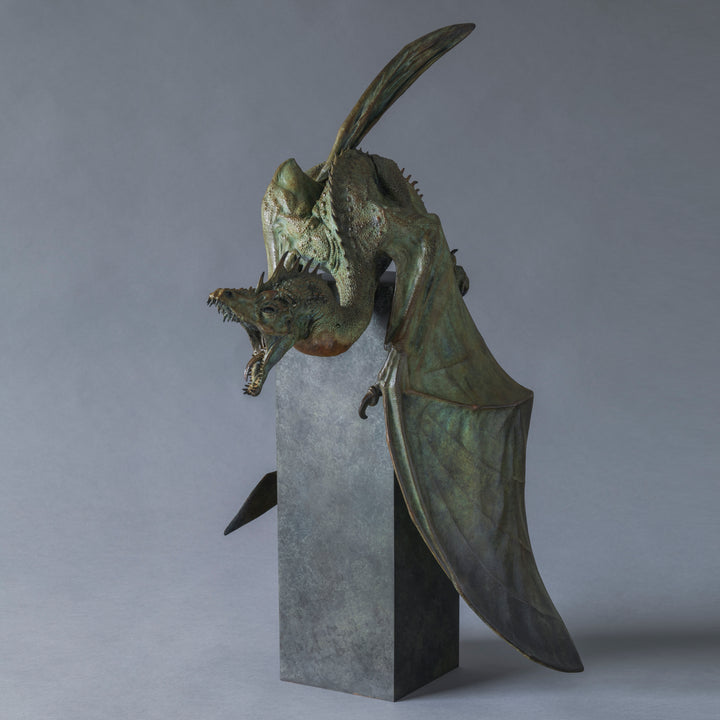 Bronze Firedrake dragon maquette by Nick Bibby, shown mid-leap with outstretched wings, spined tail and verdigris patina, blending anatomical realism with dramatic, creature-like detailing on a tall textured plinth.