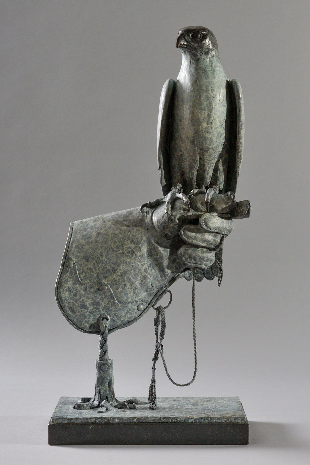 Bronze sculpture of a falcon perched on a gloved hand, finely detailed with textured surface and traditional falconry elements