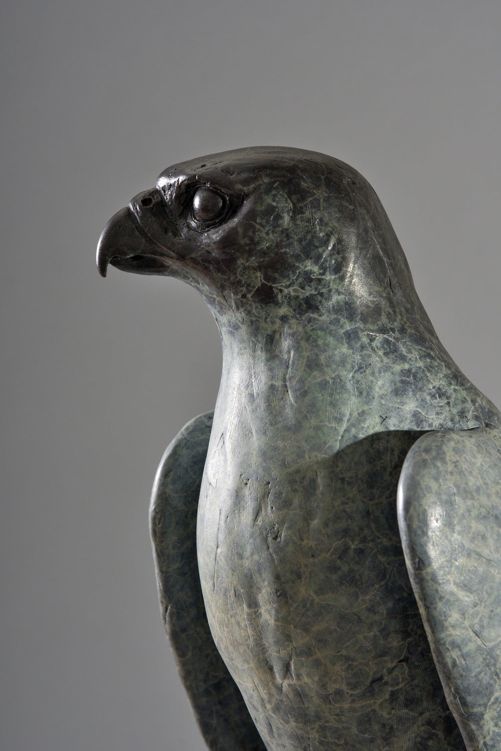 Bronze sculpture of a falcon perched on a gloved hand, finely detailed with textured surface and traditional falconry elements