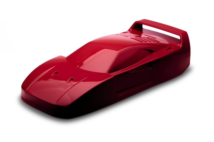 ‘Ferrari F40’ by Srini Gandra, a limited-edition contemporary automotive sculpture from the Forme di Velocità series, inspired by the legendary Ferrari F40, the final Ferrari personally approved by Enzo Ferrari. Presented in a striking high-gloss Rosso Corsa red finish, the sculpture captures the supercar's low wedge-shaped profile, sculpted bonnet, aerodynamic side intakes, distinctive rear engine vents and iconic elevated rear wing. Its smooth, minimalist surfaces celebrate the raw performance, aerodynami