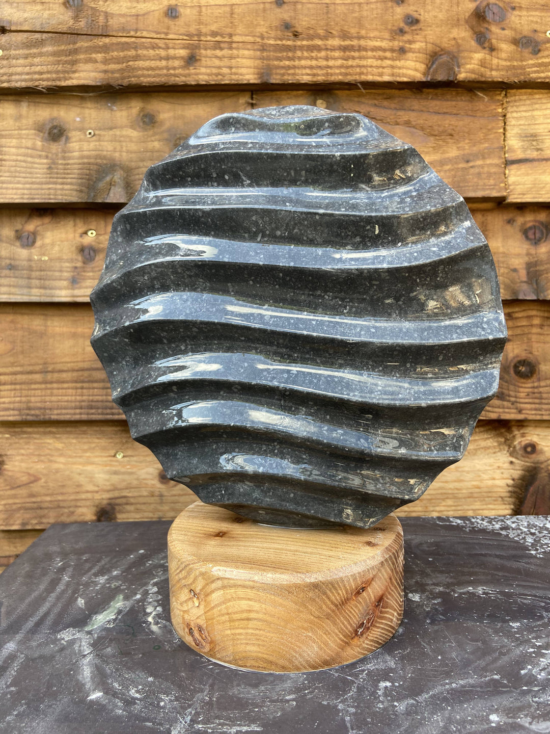 Flow 2 by Brendan Cullen, a compact hand-carved Kilkenny limestone sculpture with undulating wave-like ridges across its circular form, set on a smooth round wooden base.