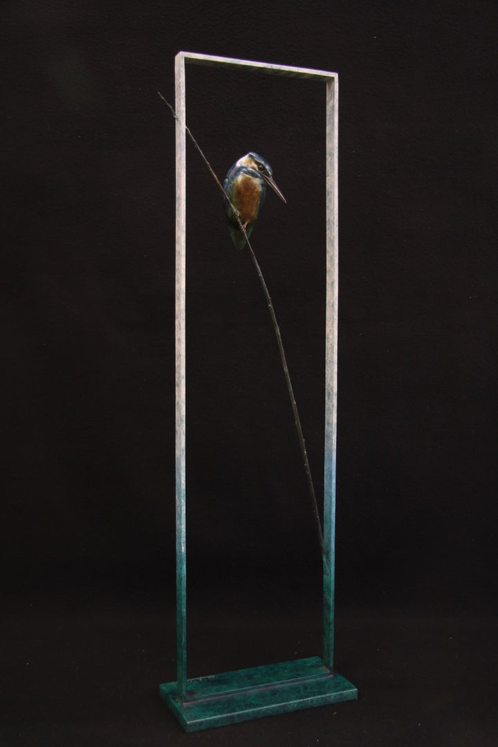 Bronze sculpture of a kingfisher perched on a slender diagonal branch within a tall rectangular frame, featuring vivid blue, turquoise, green, and amber tones.