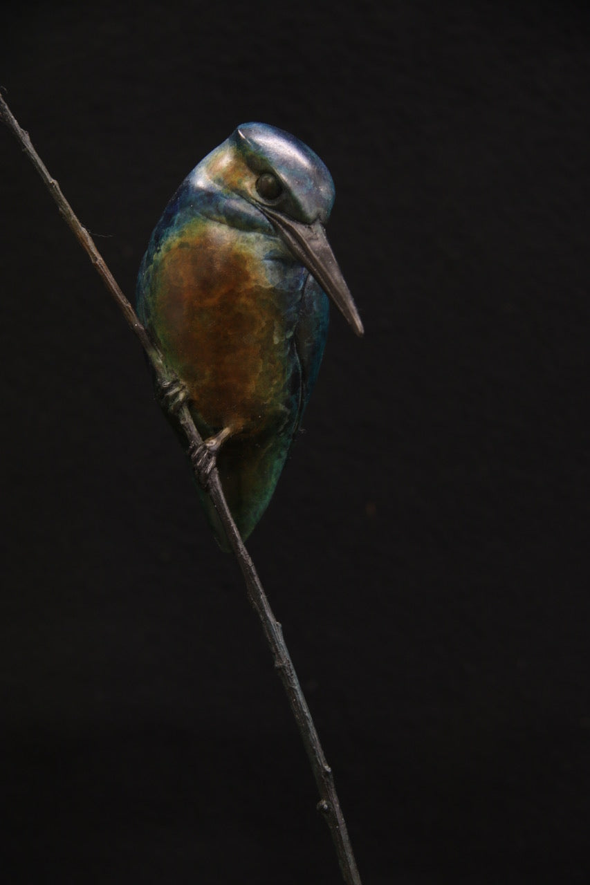 Bronze sculpture of a kingfisher perched on a slender diagonal branch within a tall rectangular frame, featuring vivid blue, turquoise, green, and amber tones.