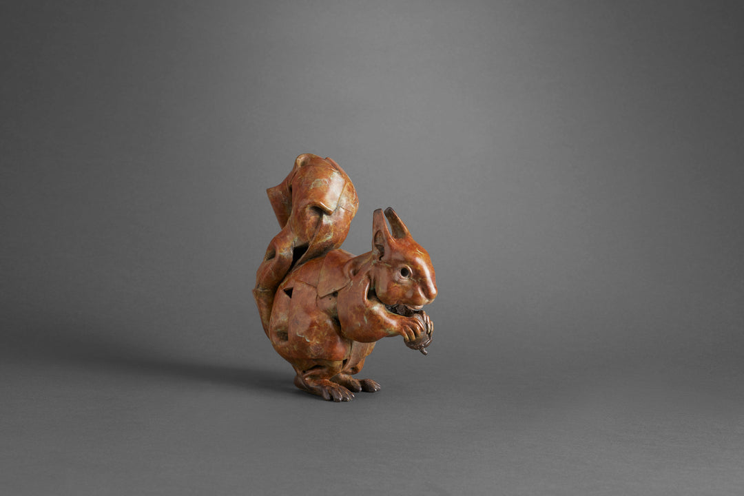 Limited edition bronze sculpture of a red squirrel by British sculptor Fred Gordon. The piece captures the squirrel in a lively pose, clutching an acorn with its detailed paws and curling tail arched high above its back. The bronze surface has a rich reddish-brown patina with subtle green and dark highlights, giving depth and movement to the form. Signed, numbered, and cast in a small edition of 25.
