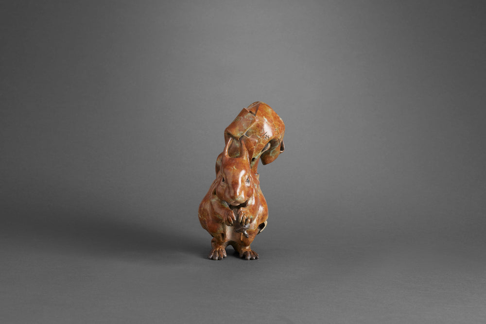 Limited edition bronze sculpture of a red squirrel by British sculptor Fred Gordon. The piece captures the squirrel in a lively pose, clutching an acorn with its detailed paws and curling tail arched high above its back. The bronze surface has a rich reddish-brown patina with subtle green and dark highlights, giving depth and movement to the form. Signed, numbered, and cast in a small edition of 25.