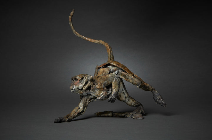 Limited edition bronze sculpture of a running macaque by British sculptor Fred Gordon. The piece captures the primate mid-stride with one arm reaching forward, legs bent in motion, and tail raised in a dynamic arc. The surface is richly textured, with earthy bronze patina tones of brown, black, and green, accented by subtle reddish highlights around the face. A signed and numbered edition of 12, the sculpture embodies movement, vitality, and raw energy in bronze form.