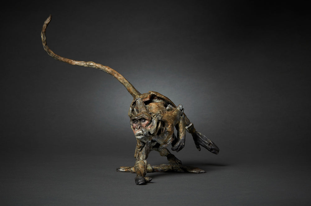 Limited edition bronze sculpture of a running macaque by British sculptor Fred Gordon. The piece captures the primate mid-stride with one arm reaching forward, legs bent in motion, and tail raised in a dynamic arc. The surface is richly textured, with earthy bronze patina tones of brown, black, and green, accented by subtle reddish highlights around the face. A signed and numbered edition of 12, the sculpture embodies movement, vitality, and raw energy in bronze form.