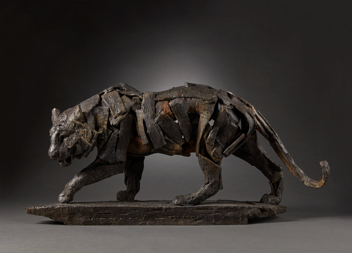 Limited edition bronze sculpture of a walking tiger by Fred Gordon. The piece shows the tiger mid-stride, muscles and movement captured through layered bronze planes that give a sense of both strength and fluidity. Rich dark patinas with earthy highlights emphasise the texture of the bronze, evoking the raw power and grace of this endangered predator. Signed and numbered in an edition of 12, the sculpture blends realism with abstraction, making it a striking wildlife artwork.