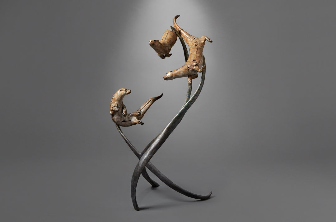 Large bronze wildlife sculpture by Fred Gordon titled Diving Otters. The piece features four otters in dynamic motion, twisting and diving around tall, fluid bronze stems that evoke both water currents and reeds. Each otter is captured mid-leap, with finely observed anatomy and playful expressions, celebrating the agility and character of these aquatic animals. Standing 160cm high, this monumental limited edition sculpture of 9 is signed and numbered, combining realism to create a striking statement piece.