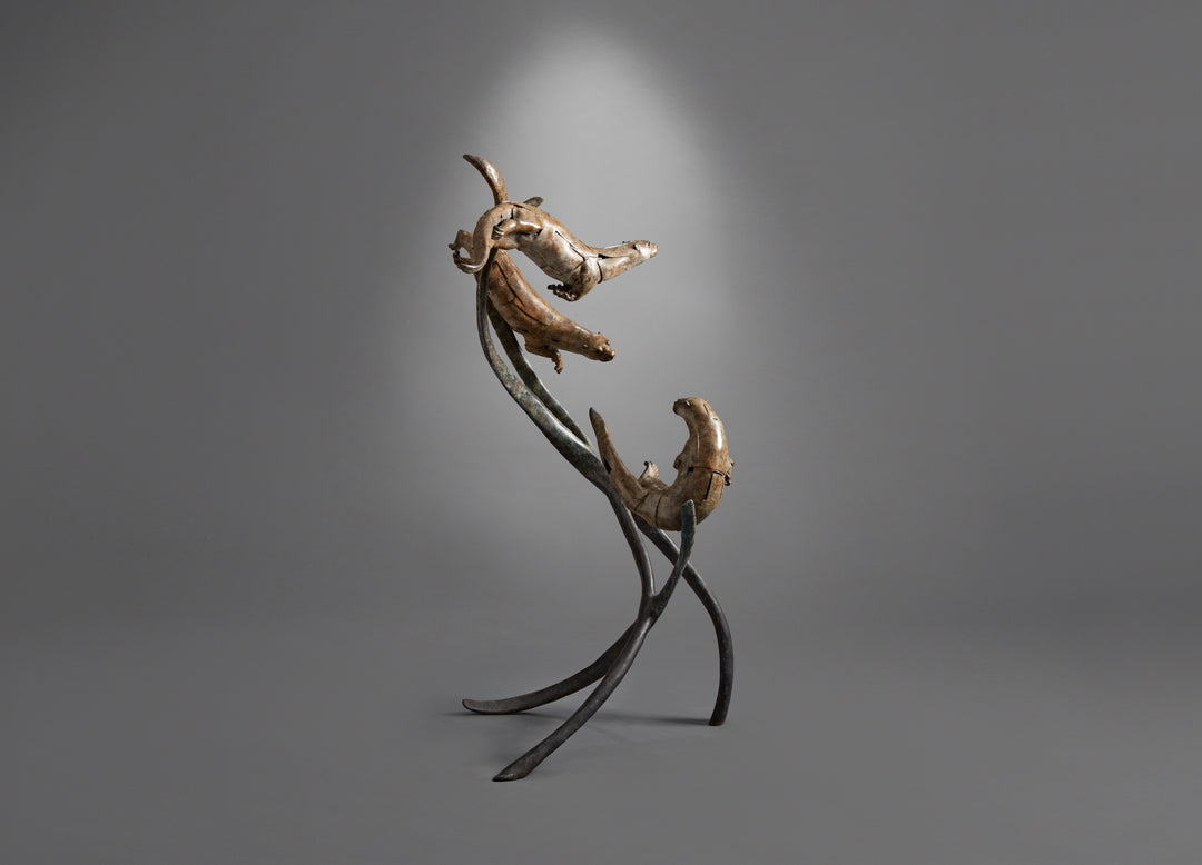 Large bronze wildlife sculpture by Fred Gordon titled Diving Otters. The piece features four otters in dynamic motion, twisting and diving around tall, fluid bronze stems that evoke both water currents and reeds. Each otter is captured mid-leap, with finely observed anatomy and playful expressions, celebrating the agility and character of these aquatic animals. Standing 160cm high, this monumental limited edition sculpture of 9 is signed and numbered, combining realism to create a striking statement piece.