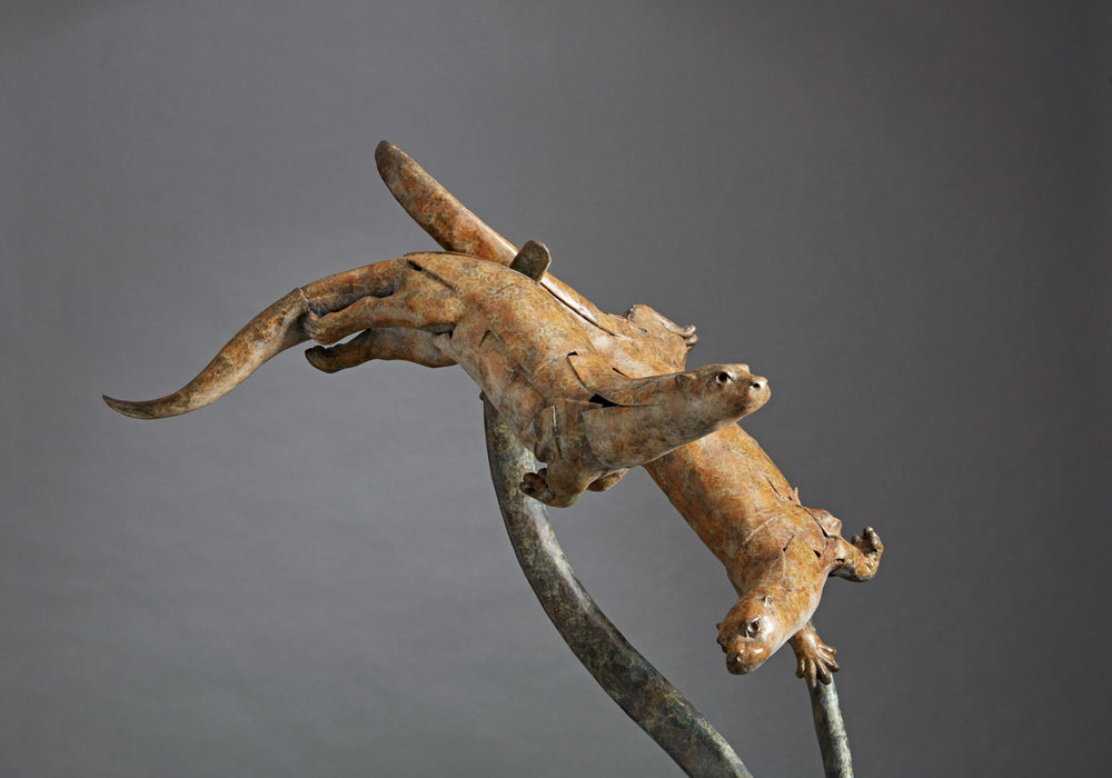 Large bronze wildlife sculpture by Fred Gordon titled Diving Otters. The piece features four otters in dynamic motion, twisting and diving around tall, fluid bronze stems that evoke both water currents and reeds. Each otter is captured mid-leap, with finely observed anatomy and playful expressions, celebrating the agility and character of these aquatic animals. Standing 160cm high, this monumental limited edition sculpture of 9 is signed and numbered, combining realism to create a striking statement piece.