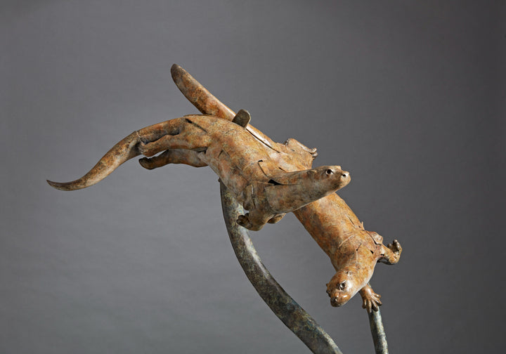 Large bronze wildlife sculpture by Fred Gordon titled Diving Otters. The piece features four otters in dynamic motion, twisting and diving around tall, fluid bronze stems that evoke both water currents and reeds. Each otter is captured mid-leap, with finely observed anatomy and playful expressions, celebrating the agility and character of these aquatic animals. Standing 160cm high, this monumental limited edition sculpture of 9 is signed and numbered, combining realism to create a striking statement piece.