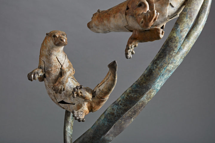 Large bronze wildlife sculpture by Fred Gordon titled Diving Otters. The piece features four otters in dynamic motion, twisting and diving around tall, fluid bronze stems that evoke both water currents and reeds. Each otter is captured mid-leap, with finely observed anatomy and playful expressions, celebrating the agility and character of these aquatic animals. Standing 160cm high, this monumental limited edition sculpture of 9 is signed and numbered, combining realism to create a striking statement piece.