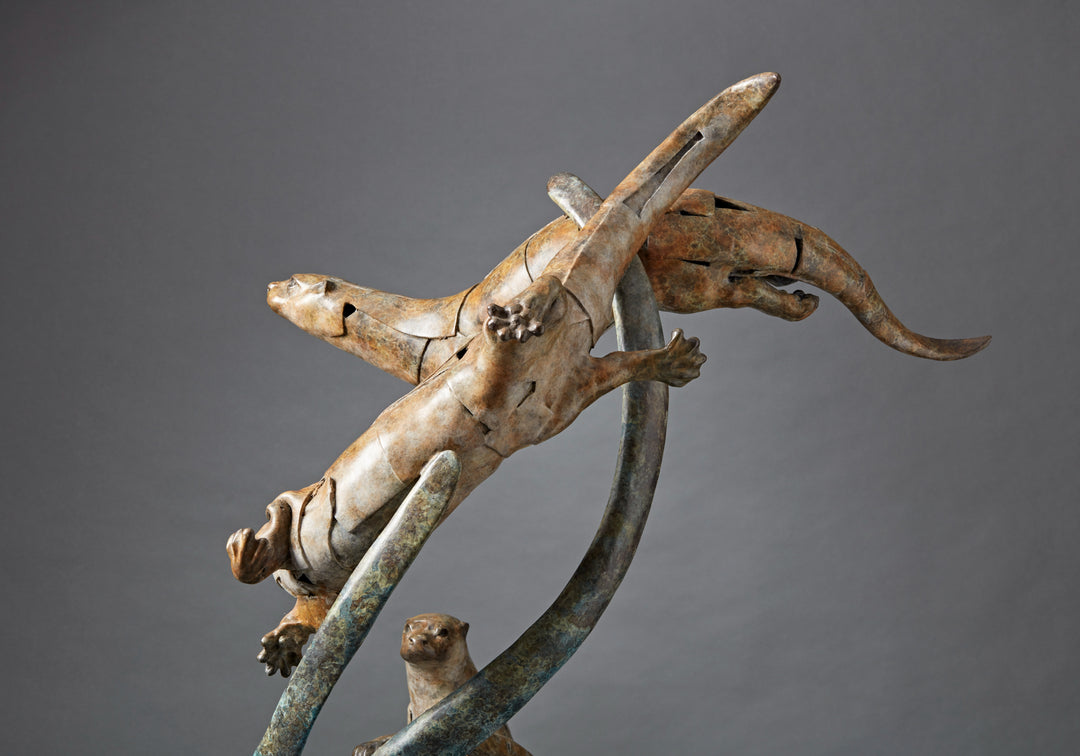 Large bronze wildlife sculpture by Fred Gordon titled Diving Otters. The piece features four otters in dynamic motion, twisting and diving around tall, fluid bronze stems that evoke both water currents and reeds. Each otter is captured mid-leap, with finely observed anatomy and playful expressions, celebrating the agility and character of these aquatic animals. Standing 160cm high, this monumental limited edition sculpture of 9 is signed and numbered, combining realism to create a striking statement piece.
