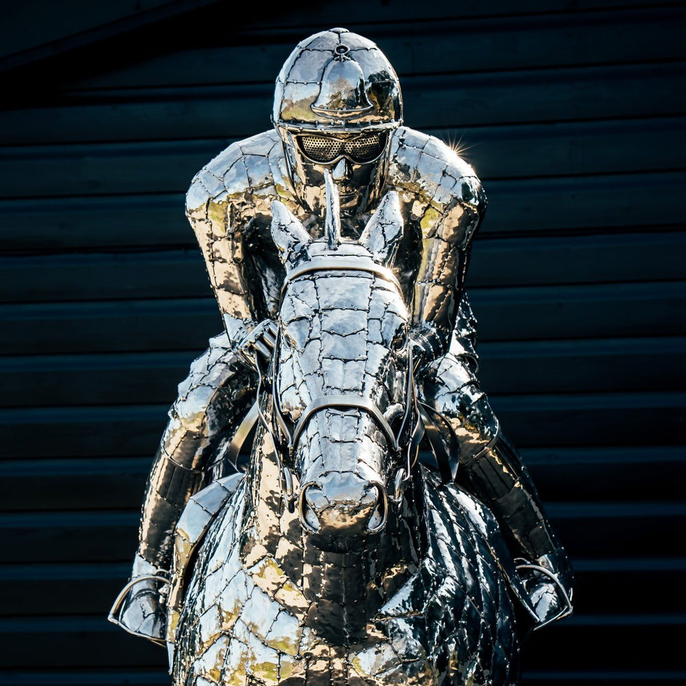 ‘Racehorse & Jockey - A Dynamic Force’ by Michael Turner, a unique, one-of-one stainless steel equestrian sculpture depicting a powerful thoroughbred racehorse galloping at full speed with its jockey leaning forward in a racing position. Handcrafted from hundreds of individually shaped and welded marine-grade stainless steel pieces, the sculpture features a polished silver finish, detailed muscular anatomy, flowing mane and tail, and a helmeted jockey holding the reins. Accompanied by a small running bird, 